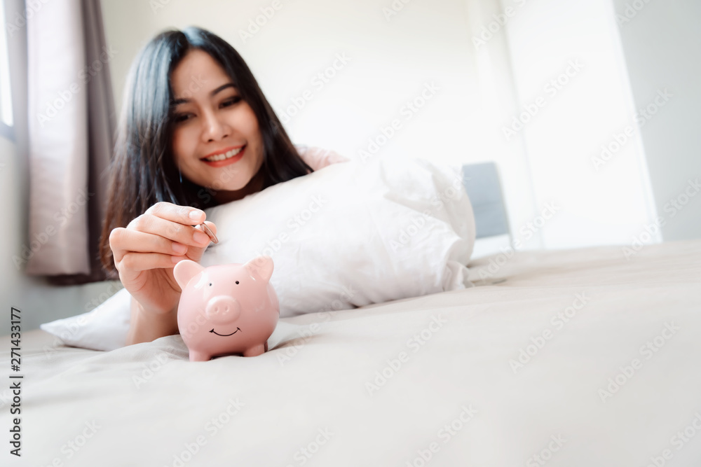 Business Banking Deposit and Financial Investing Saving Concept, Close-Up Woman Hand is Putting a Money Coin into Piggy Bank Savings for Estate Investment on The Bedroom, Retirement Interest Income Business Banking Deposit and Financial Investing Saving Concept, Close-Up Woman Hand is Putting a Money Coin into Piggy Bank Savings for Estate Investment on The Bedroom, Retirement Interest Income
