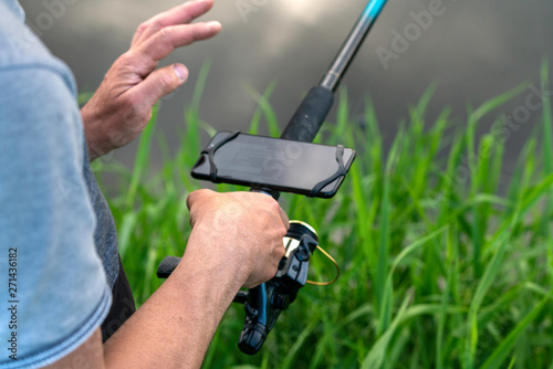 Close-up on the hand of an anglerfish measuring the depth of water in the river. On the display of the smartphone attached to the fishing rod, it reads the measurement results.