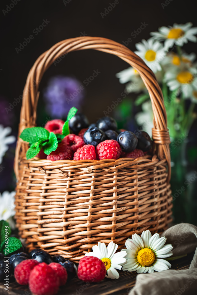 Raspberries and blueberries in a basket with chamomile and leaves on a dark background. Summer and healthy food concept. Selective focus. Background with copy space. Raspberries and blueberries in a basket with chamomile and leaves on a dark background. Summer and healthy food concept. Selective focus. Background with copy space.