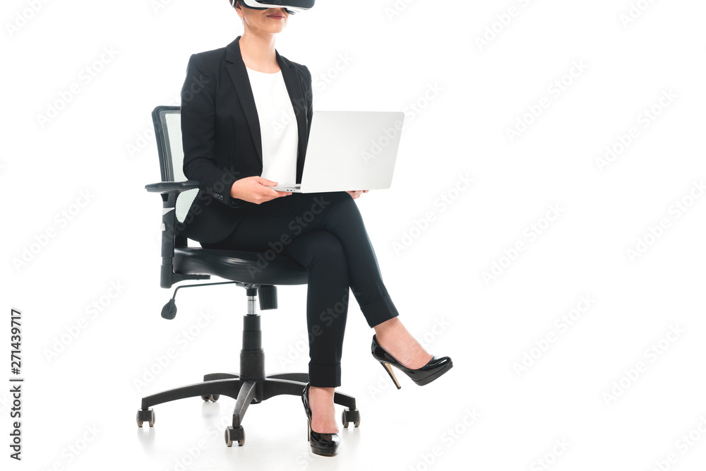 partial view of mixed race businesswoman using virtual reality headset while sitting in office chair and using laptop on white background