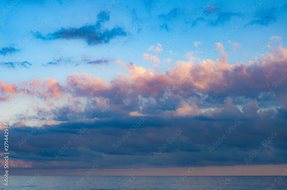 Gorgeous picturesque cloudscape above sunset calm sea in violet dusk evening with blue and lilac clouds in clear light blue sky with touch of pink. Seascape of Black sea coast. Summer cloud landscape 