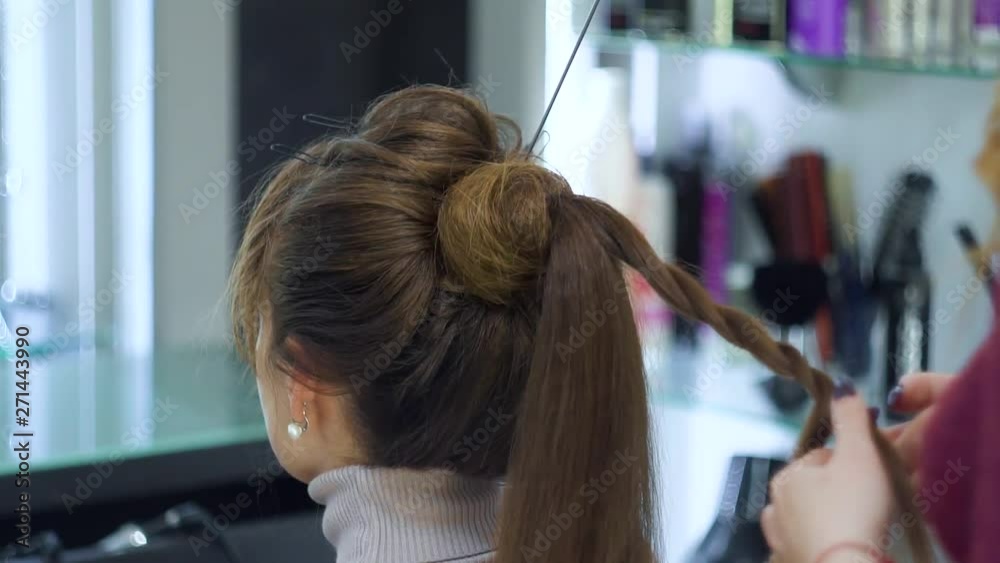 The hairdresser forms a tourniquet of two hair strips. The hairdresser makes a fashionable festive hairstyle on long, light hair The hairdresser forms a tourniquet of two hair strips. The hairdresser makes a fashionable festive hairstyle on long, light hair