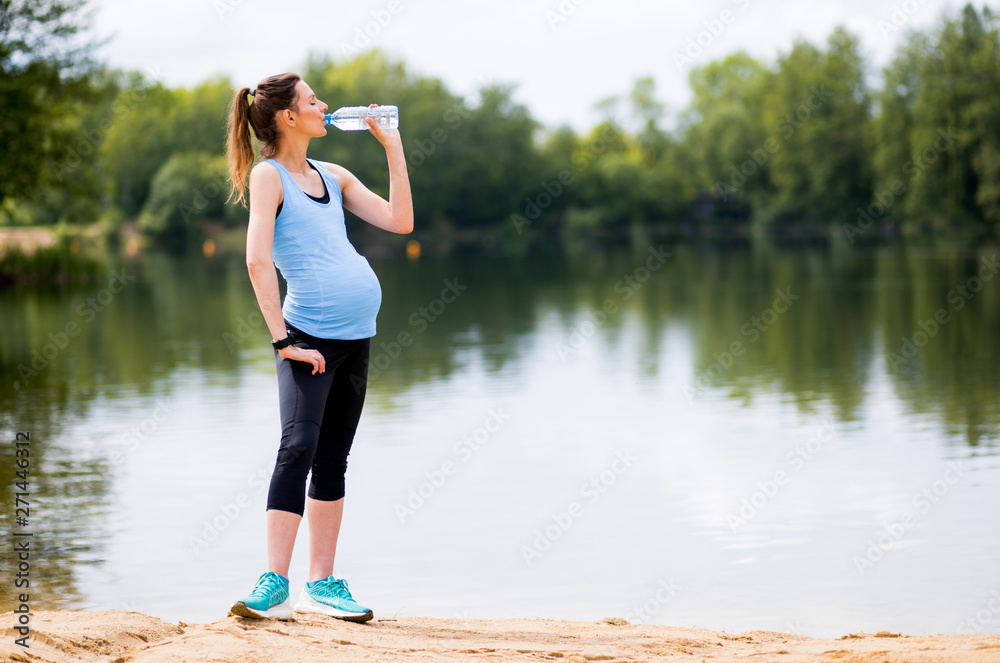 Tired pregnant woman after fitness exercises holding bottle of water outdoor