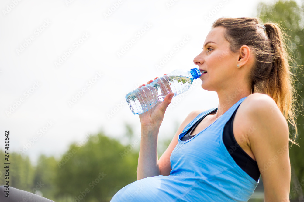 Pregnant woman resting and drinking water after fitness exercises outdoor Pregnant woman resting and drinking water after fitness exercises outdoor