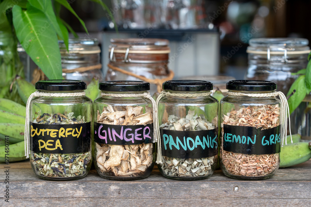 Assortment of dried spices in glass bottles on wooden background. Dry ginger, pandanus, lemon grass and butterfly pea in glass jars, closeup Assortment of dried spices in glass bottles on wooden background. Dry ginger, pandanus, lemon grass and butterfly pea in glass jars, closeup