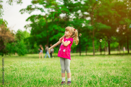 Little girl playing on the meadow on sun with windmill in her hands. Child holding wind toy on wheat field. © Svetlana