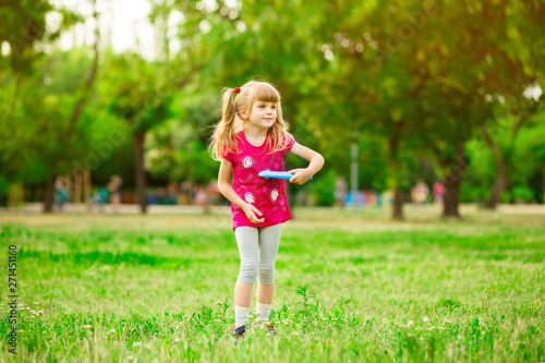 Child girl playing with a frisbee in summer park