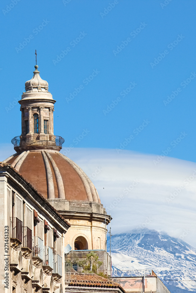 Vertical photography capturing the beautiful cupola of Roman Catholic Cathedral of Saint Agatha in Catania, Sicily, Italy. In background famous volcano Mount Etna with snow on the top