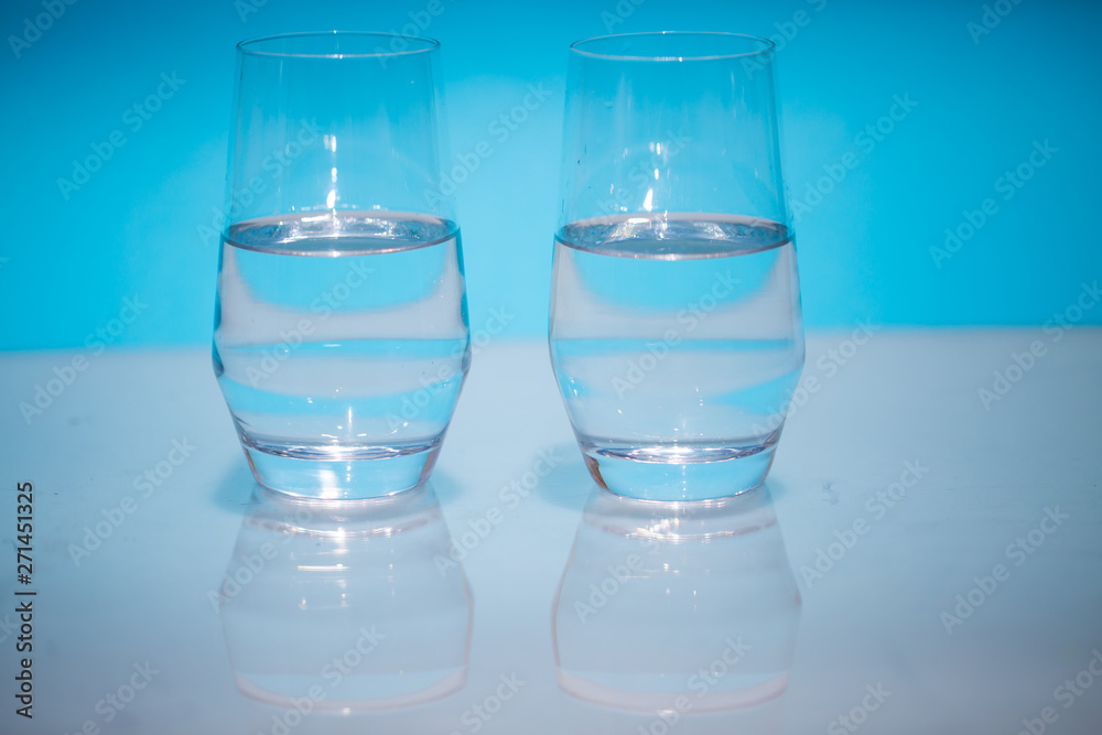 Half-full water glasses, two half-empty water glasses against a blue background Half-full water glasses, two half-empty water glasses against a blue background