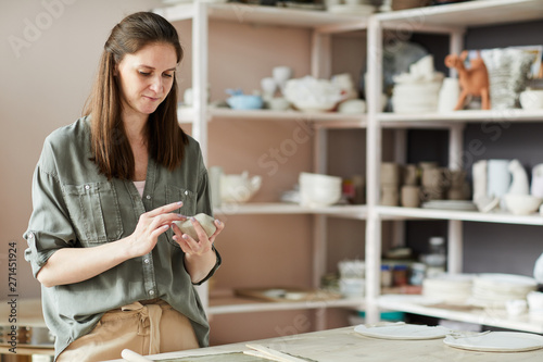 Waist up portrait of contemporary female artisan working in pottery studio, copy space