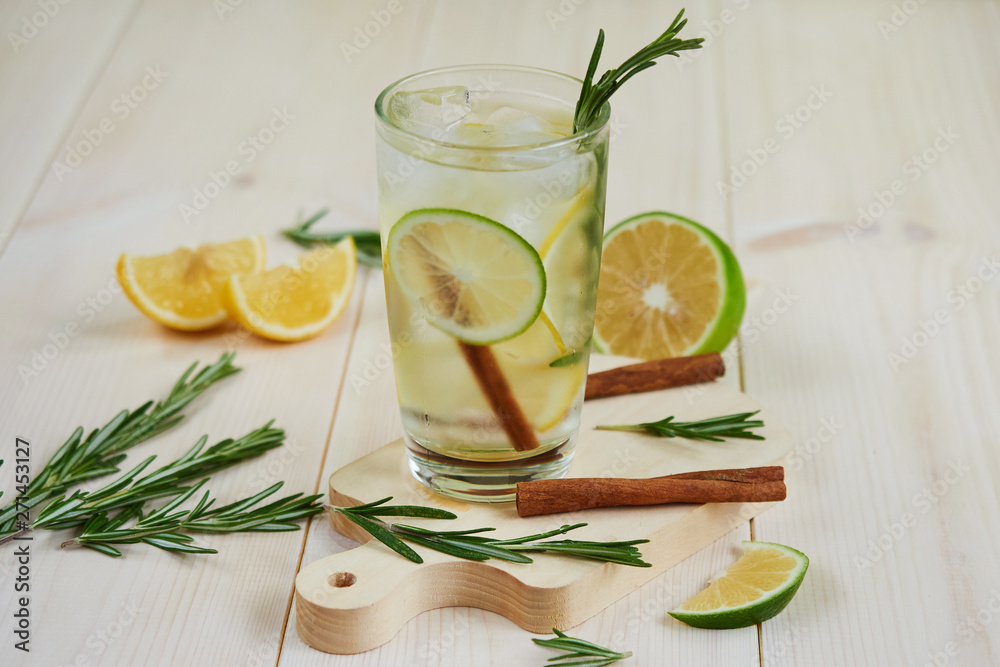 Fototapeta premium lemonade with fresh lemon, lime, decorated with a rosemary branch on a light wooden background