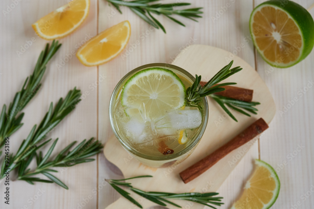a glass of lemonade with fresh lemon, lime, decorated with a rosemary branch on a light wooden background, view from above a glass of lemonade with fresh lemon, lime, decorated with a rosemary branch on a light wooden background, view from above