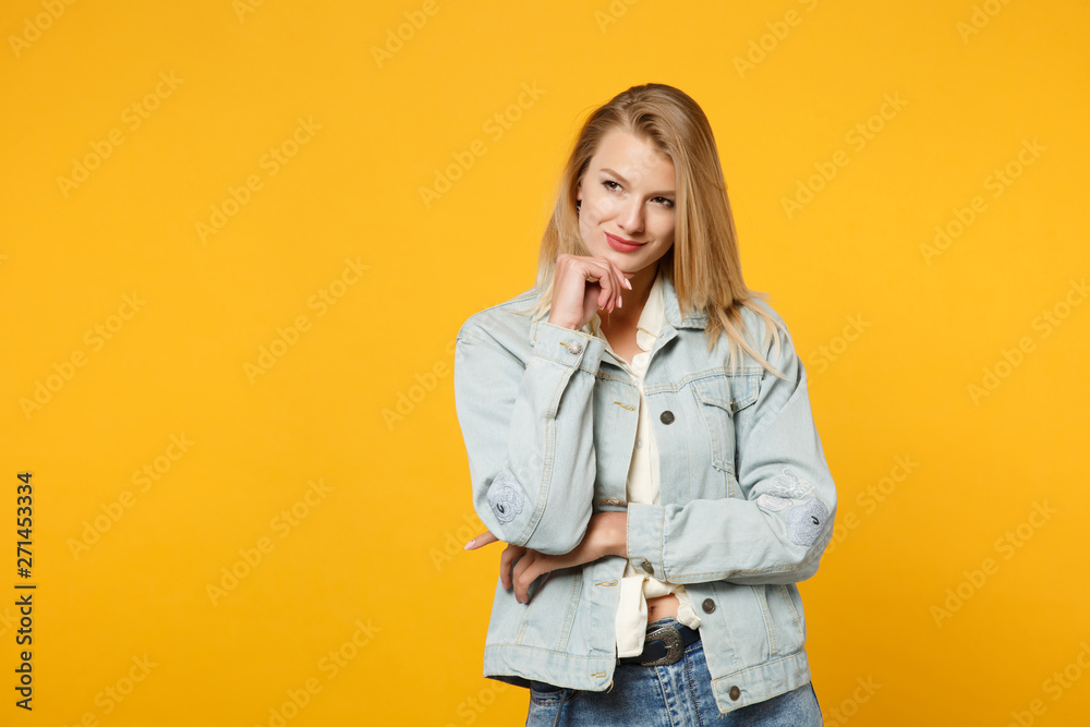 Portrait of charming smiling young woman in denim casual clothes put hand prop up on chin, looking aside isolated on yellow orange background in studio. People lifestyle concept. Mock up copy space. Portrait of charming smiling young woman in denim casual clothes put hand prop up on chin, looking aside isolated on yellow orange background in studio. People lifestyle concept. Mock up copy space.