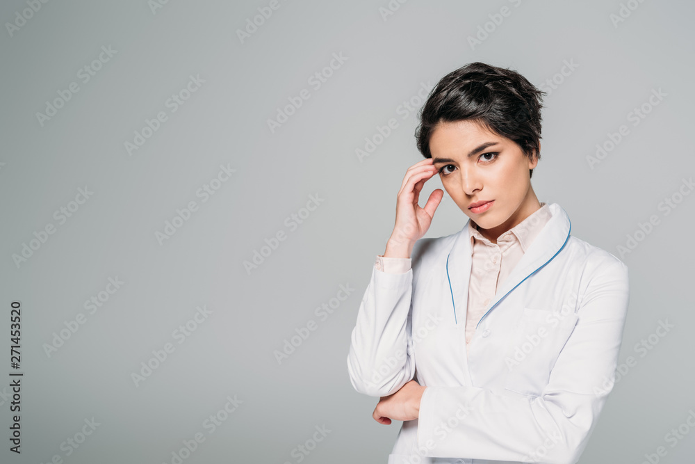 pensive mixed race doctor looking at camera while holding hand near head isolated on grey pensive mixed race doctor looking at camera while holding hand near head isolated on grey
