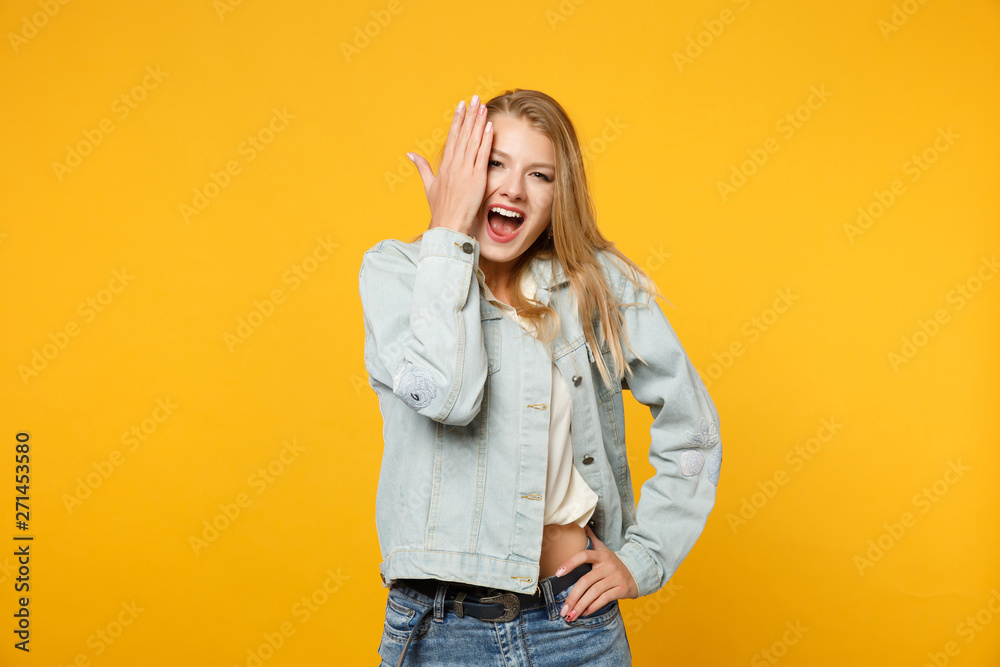 Obraz premium Excited funny screaming young woman in denim casual clothes looking camera, covering face with hand isolated on bright yellow orange background in studio. People lifestyle concept. Mock up copy space.