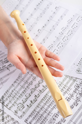 Plastic beige flute in the children's hand on the background of sheets with musical notes