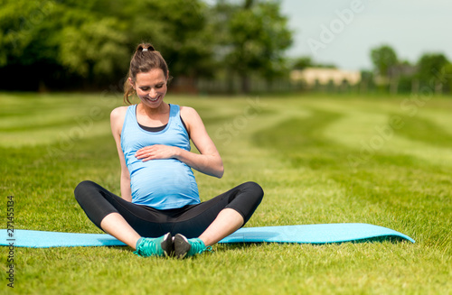 Pregnant woman fitness exercises on grass at sunny day