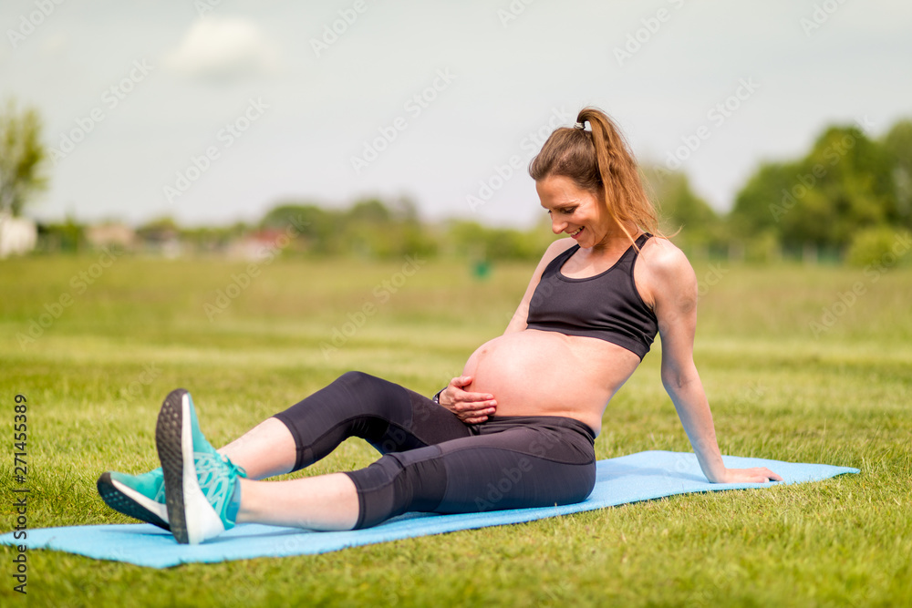 Pregnant woman fitness exercises on grass at sunny day Pregnant woman fitness exercises on grass at sunny day