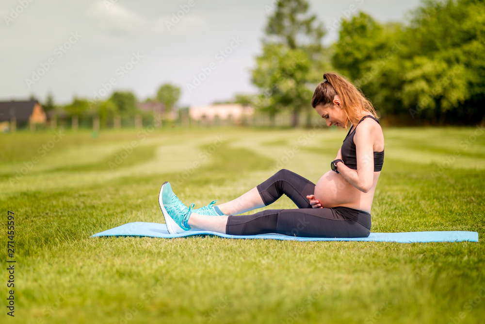 Pregnant woman fitness exercises on grass at sunny day Pregnant woman fitness exercises on grass at sunny day