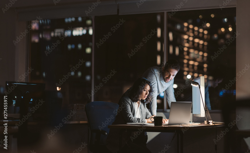 Young business colleagues working overtime together at an office desk - obrazy, fototapety, plakaty 