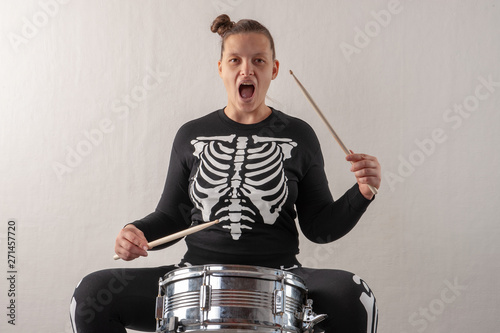 Happy attractive woman of musician in carnival costume, young mother play drum and try to sing. Black suit with image of skeletons. Classic halloween costume. Funny crazy girl photo