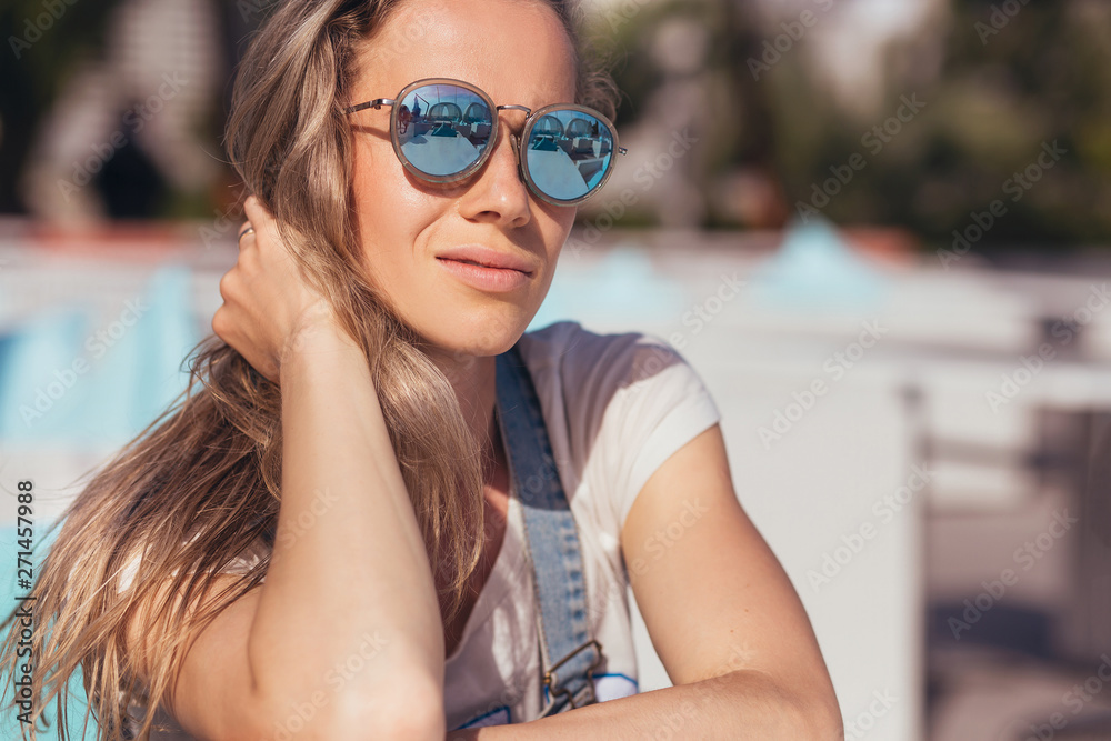 Close-up dreamy satisfied woman tourist in sunglasses smiling looking at camera on a sunny summer day while relaxing in the sun by the sea on a hot sunny day Close-up dreamy satisfied woman tourist in sunglasses smiling looking at camera on a sunny summer day while relaxing in the sun by the sea on a hot sunny day
