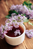 branches of blooming lilacs and a cup of tea on a wooden background