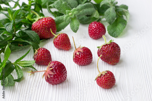 Red strawberries  fresh mint and melissa herbs on white wood