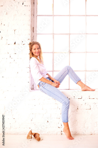 Confident blond woman wearing casual clothes while posing by the window