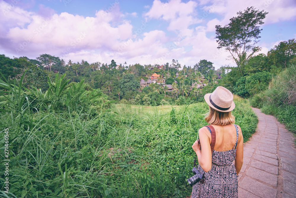 Tropical travel. Young woman in hat with camera enjoying jungle view.