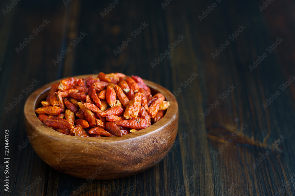 Dried bird's eye chili peppers in a wooden bowl. Dark wooden table, high resolution, negative space Dried bird's eye chili peppers in a wooden bowl. Dark wooden table, high resolution, negative space