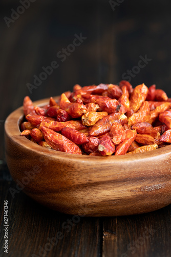 Dried bird's eye chili peppers in a wooden bowl. Dark wooden table, high resolution