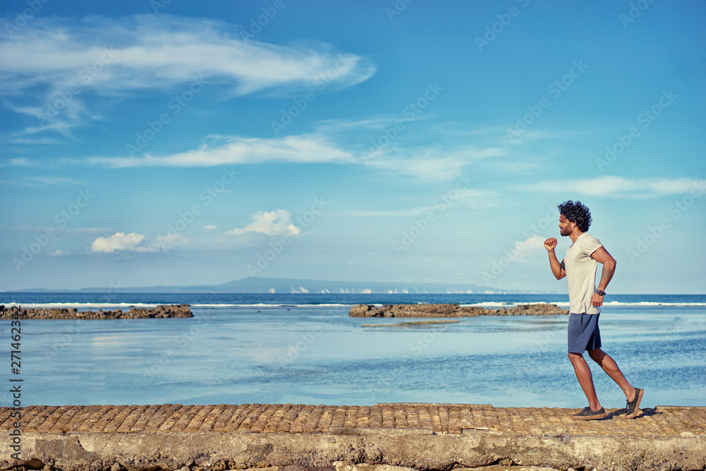 Sports lifestyle. Happy young african man jogging on the sea shore.