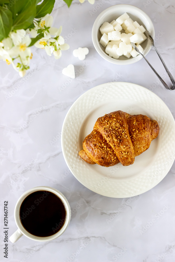 A croissant and coffee on a marble background. The flowers. Breakfast. A croissant and coffee on a marble background. The flowers. Breakfast.