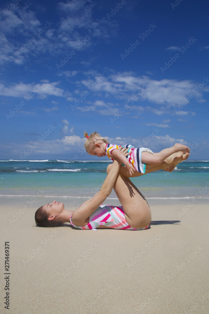 Mother doing yoga exercise together with her baby girl, outdoor family activity, family summer vacation concept Mother doing yoga exercise together with her baby girl, outdoor family activity, family summer vacation concept