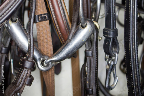 Trenzel made of metal suspended on belts of bridles, against a background of various leather harnesses close-up © Alexey Wraith