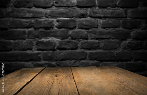 Old wood table with blurred concrete block wall in dark room background.
