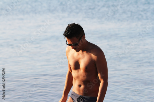 Handsome man with sunglasses and swimsuit are enjoying on the beach at sunset. Apulia, Salento, Italy