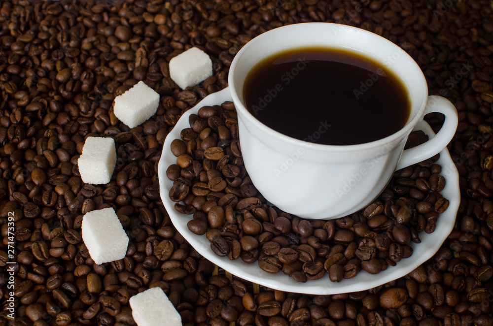 close-up of white Cup and saucer with black hot strong coffee Americano on a dark background of coffee beans with five pieces of white sugar refined. Flatlay close-up of white Cup and saucer with black hot strong coffee Americano on a dark background of coffee beans with five pieces of white sugar refined. Flatlay