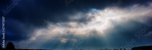dark rainy sky and bright sun rays against the background of clouds. © APHOTOSTUDIO
