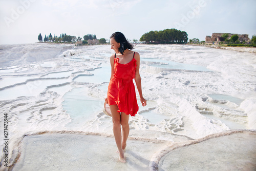 Woman in a red dress stands on white travertines. Girl in the sun near the white wall. Pamukkale