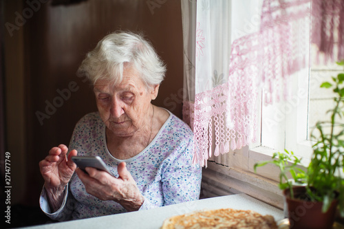 Old lady sits and typing on smartphone. Elderly people and technology.