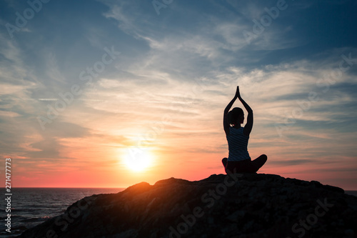 Silhouette of yoga woman sitting in Lotus position on the sea beach during fantastic sunset.