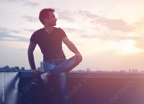 Fototapeta Naklejka Na Ścianę i Meble -  Attractive stylish young man on the roof at sunset looking at t city