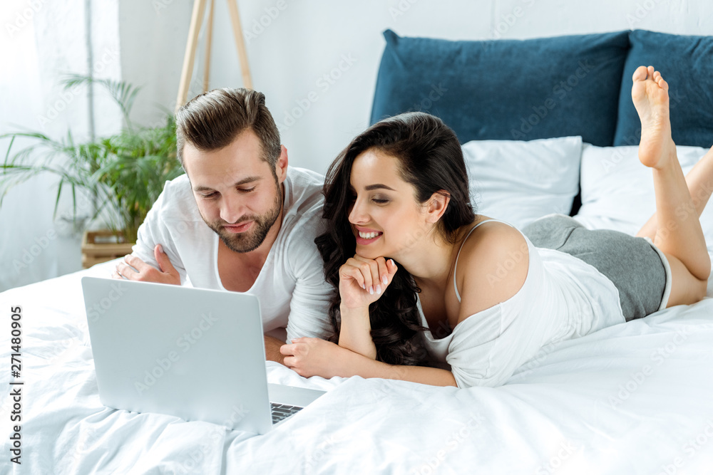 happy couple looking at laptop screen while lying in bed, illustrative editorial happy couple looking at laptop screen while lying in bed, illustrative editorial