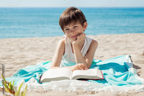 Boy with book lying on the beach a sunny day looking at camera