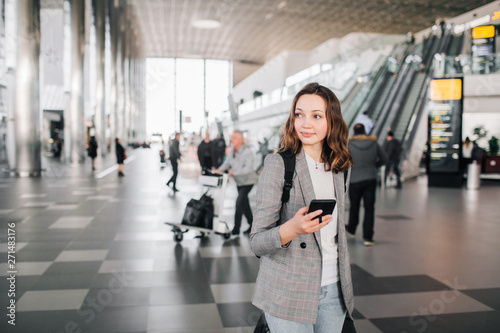 Girl at the airport, walking with her smartphone and baggage.