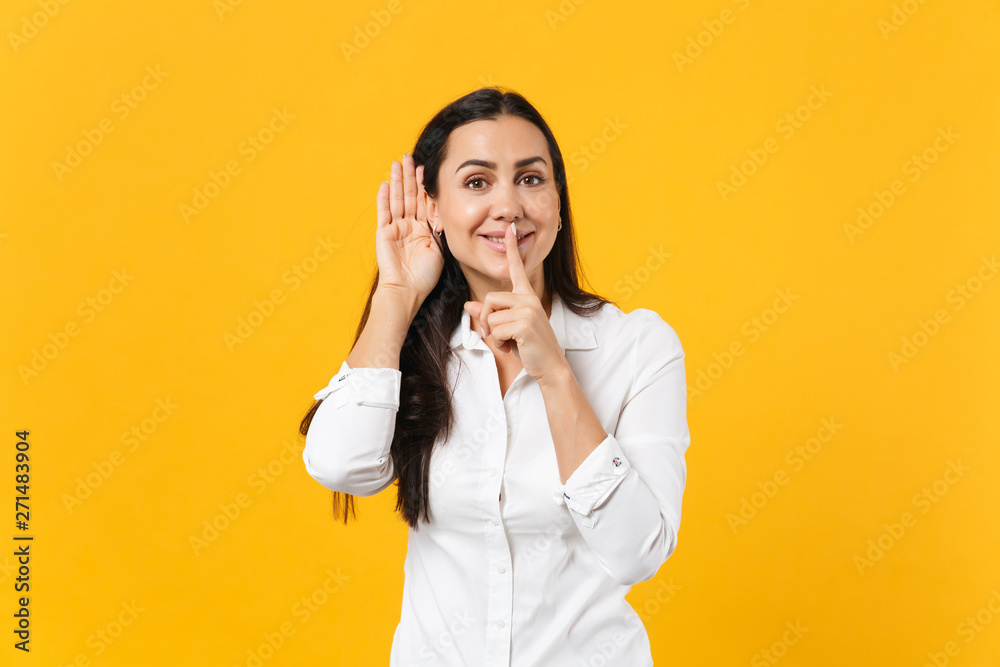 Portrait of joyful young woman in white shirt say hush be quiet with finger on lips shhh gesture, try to hear you isolated on yellow orange background. People lifestyle concept. Mock up copy space. Portrait of joyful young woman in white shirt say hush be quiet with finger on lips shhh gesture, try to hear you isolated on yellow orange background. People lifestyle concept. Mock up copy space.