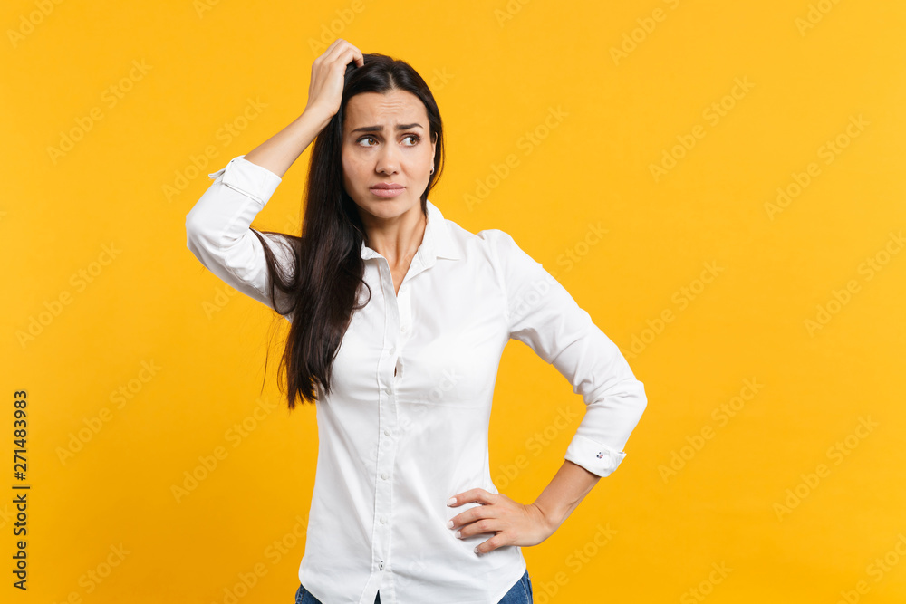 Portrait of preoccupied pensive young woman in white shirt looking aside, putting hand on head isolated on bright yellow orange wall background in studio. People lifestyle concept. Mock up copy space. Portrait of preoccupied pensive young woman in white shirt looking aside, putting hand on head isolated on bright yellow orange wall background in studio. People lifestyle concept. Mock up copy space.
