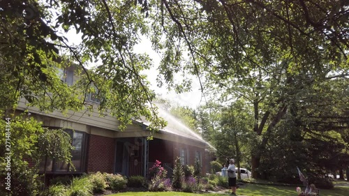 A heavy set Caucasian man sprays the siding of a house with a water based detergent in order to pressure wash it photo